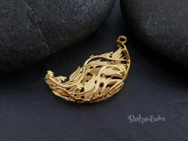 May include: Gold-toned metal pendant shaped like a leaf with intricate cut-out details. The pendant has a delicate, airy design and would be a beautiful addition to a necklace or bracelet.
