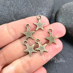 May include: Six antique gold-toned metal star charms with a loop at the top for attaching to jewelry or crafts.