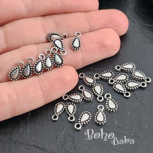 May include: A collection of silver teardrop-shaped charms with a beaded edge. The charms have a hole at the top for attaching to jewelry or other crafts.