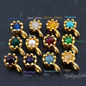 May include: Assortment of 12 gold crown charms with different coloured gemstones, including sapphire blue, opal white, citrine yellow, turquoise, pearl, emerald green, ruby red, peridot green, amethyst purple, aquamarine blue, and clear.
