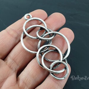 May include: Silver pendant featuring an intricate design of interlocked circles. The pendant is crafted from metal and has a textured finish.