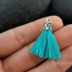 May include: Teal tassel with a silver metal top. The tassel is made of soft, thin strands of yarn and has a decorative, ornate metal top.