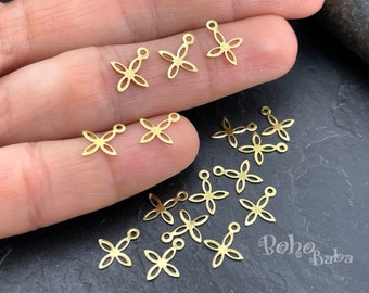 May include: A close-up of a collection of gold-toned metal flower charms with a loop at the top. The charms are scattered on a dark surface and a hand is holding some of the charms.