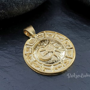 May include: Gold-toned pendant featuring a circular design with a sun and moon symbol in the center. The outer circle is decorated with zodiac symbols.