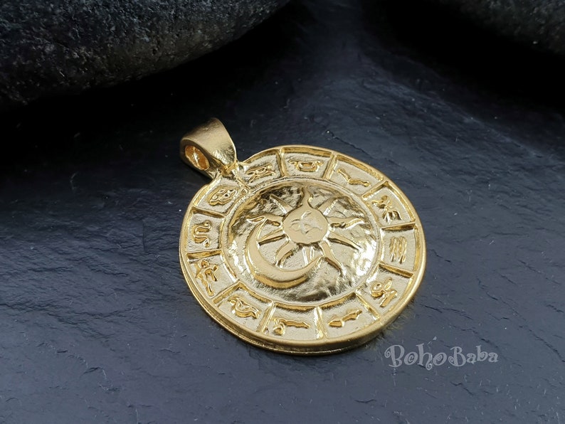 May include: Gold-toned pendant featuring a circular design with a sun and moon symbol in the center. The outer circle is decorated with zodiac symbols.
