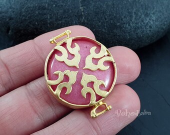 Peut inclure: Un pendentif rond en métal rose et or avec un motif décoratif complexe. Le pendentif a un fermoir de chaque côté.