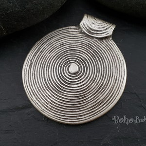 May include: Silver pendant with a circular design featuring concentric circles. The pendant has a loop at the top for attaching to a chain or cord.