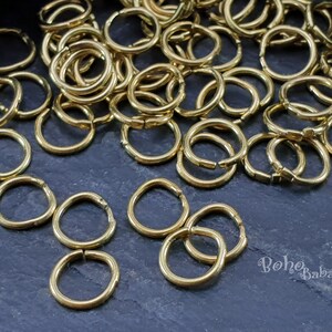 May include: A large pile of gold jump rings, with a few smaller rings scattered around. The rings are all smooth and shiny.