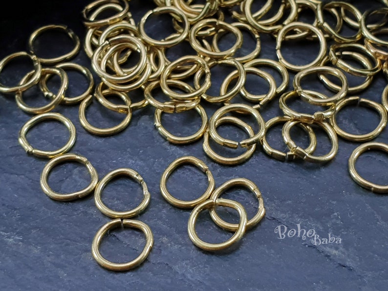 May include: A large pile of gold jump rings, with a few smaller rings scattered around. The rings are all smooth and shiny.