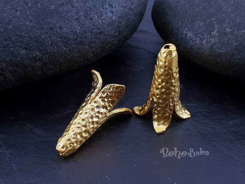 Puede incluir: Dos tapas de cuentas de metal dorado en forma de cono con textura martillada. Las tapas tienen una parte superior puntiaguda y una base acampanada con cuatro puntos.