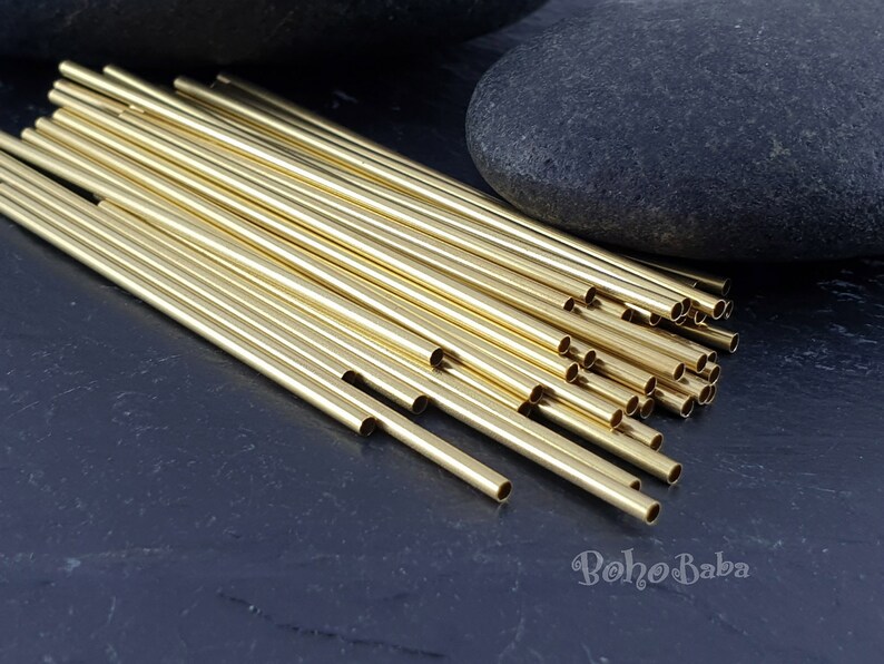 May include: A pile of gold-colored metal tubes, likely for jewelry making, on a dark gray surface. The tubes are arranged in a fan shape, with the ends of the tubes visible.