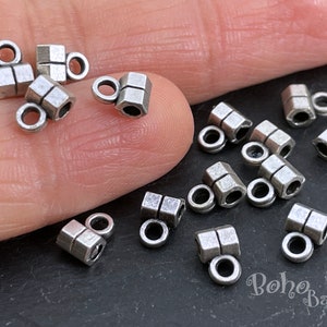 May include: Silver tone metal end caps for jewelry making. The end caps are square shaped with a small loop on one end. There are 15 end caps in the image.