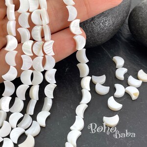 Pode incluir: Contas de madrepérola branca em forma de lua crescente. As contas são enfiadas em um cordão branco e têm um diâmetro de aproximadamente 1,2 cm. As contas são perfeitas para fazer joias ou outros artesanatos.