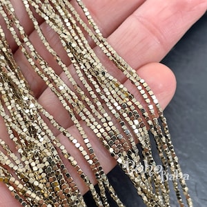 May include: Close-up of multiple strands of gold-colored, square-shaped beads. The beads are strung together, creating a delicate, shimmering effect. The beads are likely used for jewelry making or other craft projects.