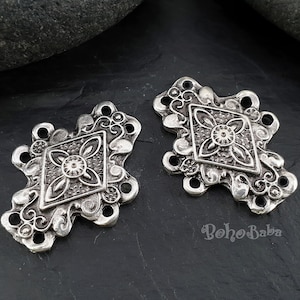 May include: Two silver-toned metal connector charms with a diamond-shaped design and intricate floral details. Each charm has four holes for attaching to jewelry or other crafts.