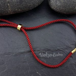 May include: A red cord bracelet with gold-toned metal accents. The bracelet has a sliding knot closure and is adjustable in size.