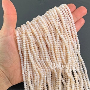 May include: A strand of white iridescent glass beads. The beads are small and round, with a faceted finish. The beads are strung on a clear thread.