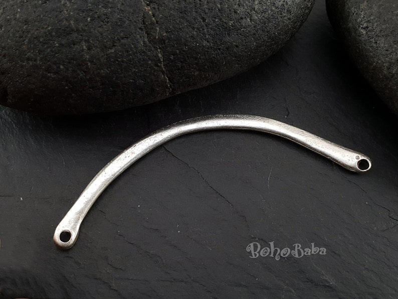 May include: Silver-toned metal connector with two holes, curved into an arc shape. The connector is on a dark gray surface.