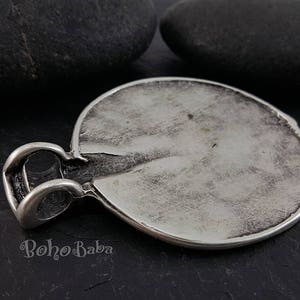 May include: A silver-toned pendant with a textured, circular design. The pendant has a loop for a chain and a slightly distressed appearance. The word "BohoBaba" is visible on the bottom of the pendant.