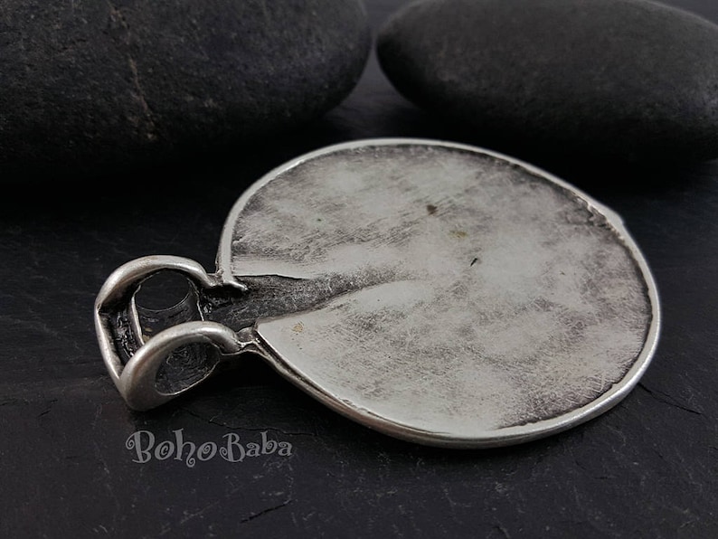 May include: A silver-toned pendant with a textured, circular design. The pendant has a loop for a chain and a slightly distressed appearance. The word "BohoBaba" is visible on the bottom of the pendant.