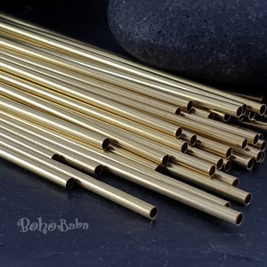 May include: A pile of gold-colored metal tubes, likely for jewelry making, on a dark blue surface. The tubes are arranged in a staggered pattern, with some of the tubes extending beyond the edge of the pile. The tubes are all the same size and shape, and they have a smooth, polished finish.