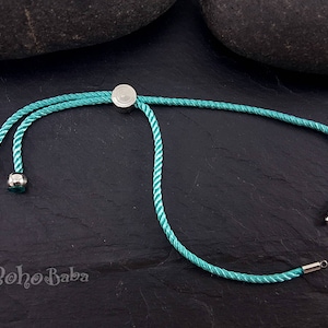 May include: A turquoise blue adjustable cord bracelet with silver metal end caps and a silver metal slider.