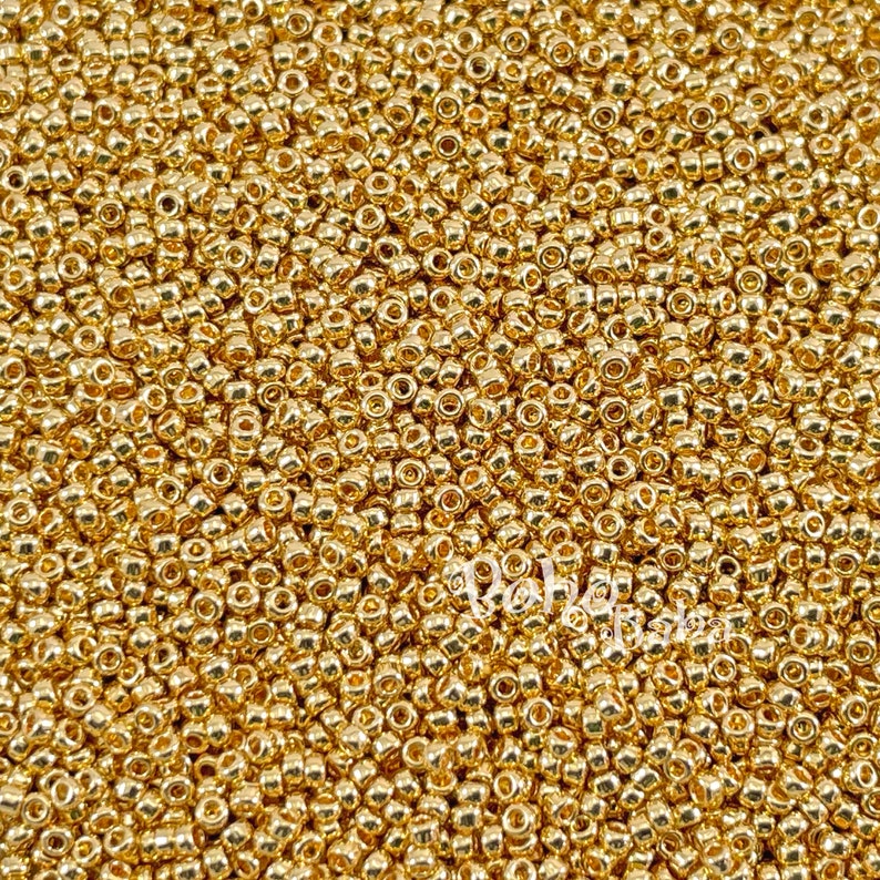 May include: A close-up view of a large quantity of small, round, gold-coloured beads. The beads are arranged in a random pattern, creating a textured surface.