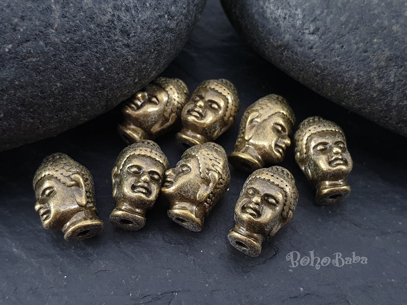 May include: A collection of eight antique gold-toned Buddha head beads. The beads are detailed with intricate carvings and have a distressed finish.