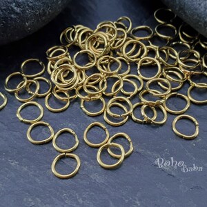 May include: A large pile of gold jump rings, a type of jewelry finding, on a dark gray background. The rings are small and round, and they are perfect for making jewelry.
