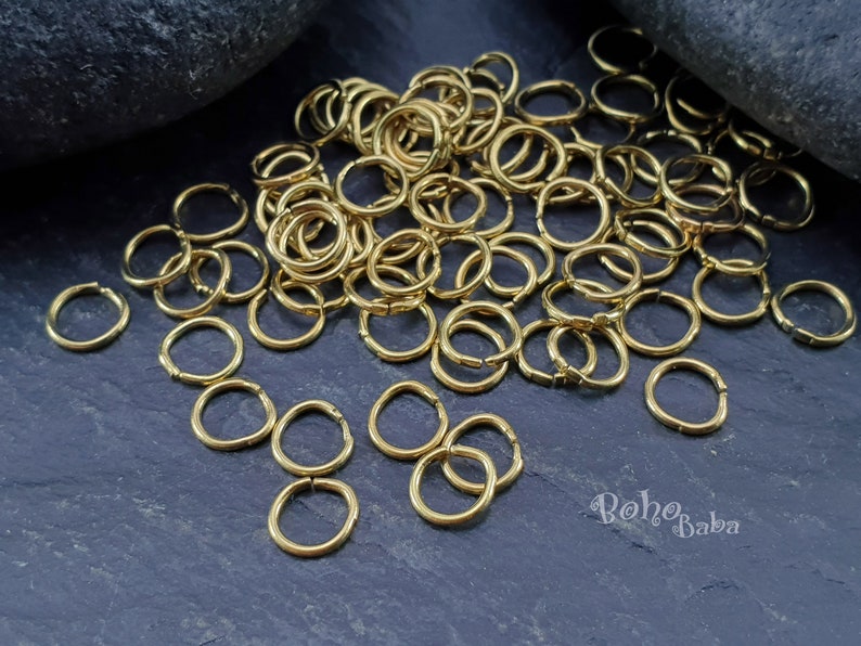 May include: A large pile of gold jump rings, a type of jewelry finding, on a dark gray background. The rings are small and round, and they are perfect for making jewelry.