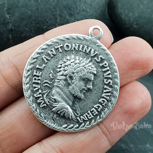 Puede incluir: Encanto de colgante de plata con el perfil de un emperador romano y la inscripción "IMP ANTONINVS PIVS AVG GERM".