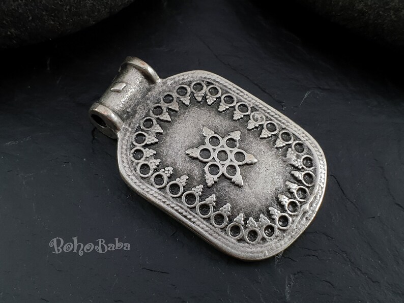 May include: Silver pendant with a star-shaped design and intricate details. The pendant has a rectangular shape with a loop at the top for attaching to a chain.
