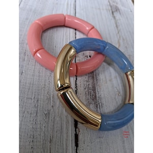 May include: Two stretch bracelets. One bracelet consists of solid, glossy, light pink cylindrical beads. The second bracelet features alternating segments of glossy, marbled light blue cylindrical beads and smooth, reflective gold-tone metal tubes.