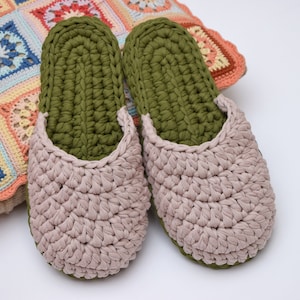 May include: A pair of crocheted slippers with a green top and a pink bottom. The slippers are sitting on a colorful crocheted pillow.