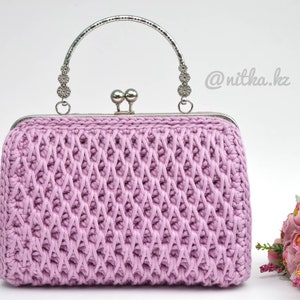 Könnte beinhalten: Eine lavendelfarbene gehäkelte Clutch mit einem silbernen Metallgriff und Verschluss. Die Tasche hat ein rautenförmiges Muster und ist mit kleinen silbernen Perlen verziert.