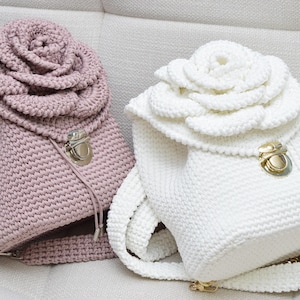 May include: Two crocheted backpacks with rose-shaped tops. One is pink and the other is white. Both have a gold metal clasp.