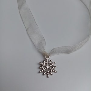 May include: A silver snowflake charm pendant on a white ribbon.