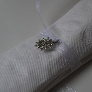 May include: A white napkin with a silver snowflake charm attached to a white ribbon.