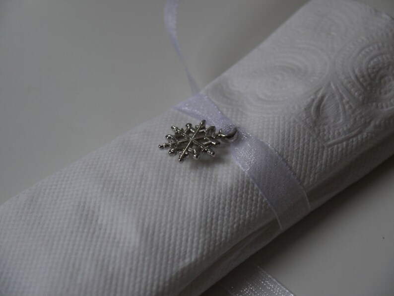 May include: A white napkin with a silver snowflake charm attached to a white ribbon.