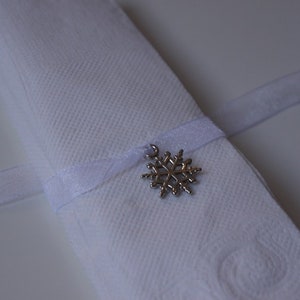 May include: A white napkin tied with a white ribbon and a silver snowflake charm.
