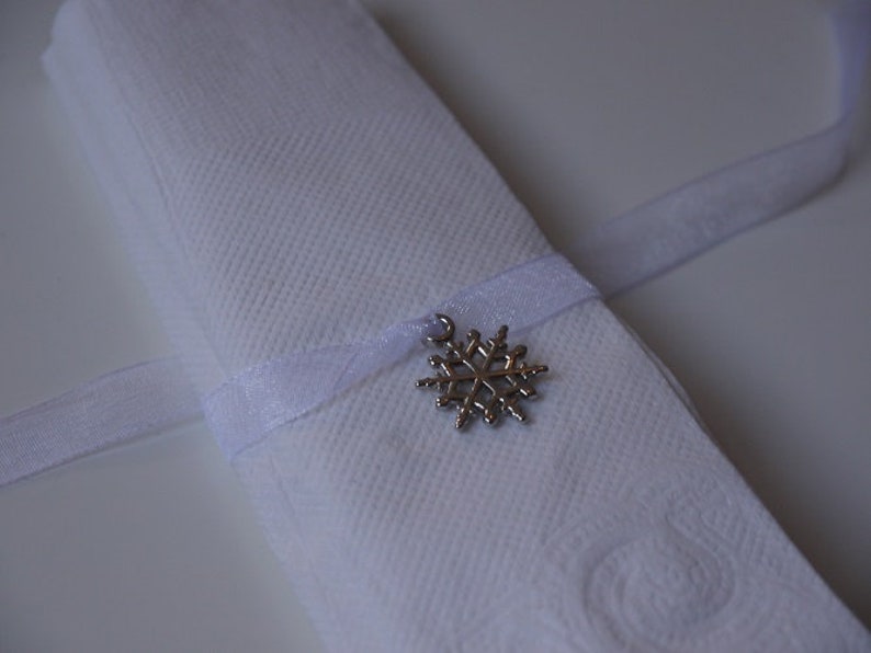 May include: A white napkin tied with a white ribbon and a silver snowflake charm.