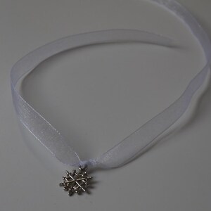 May include: A white ribbon necklace with a silver snowflake pendant.