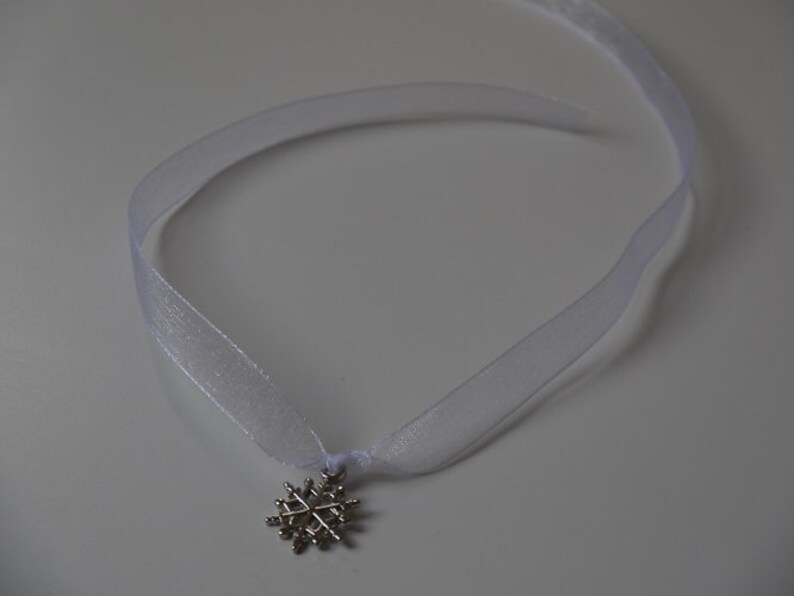 May include: A white ribbon necklace with a silver snowflake pendant.