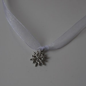May include: A white ribbon necklace with a silver snowflake pendant.