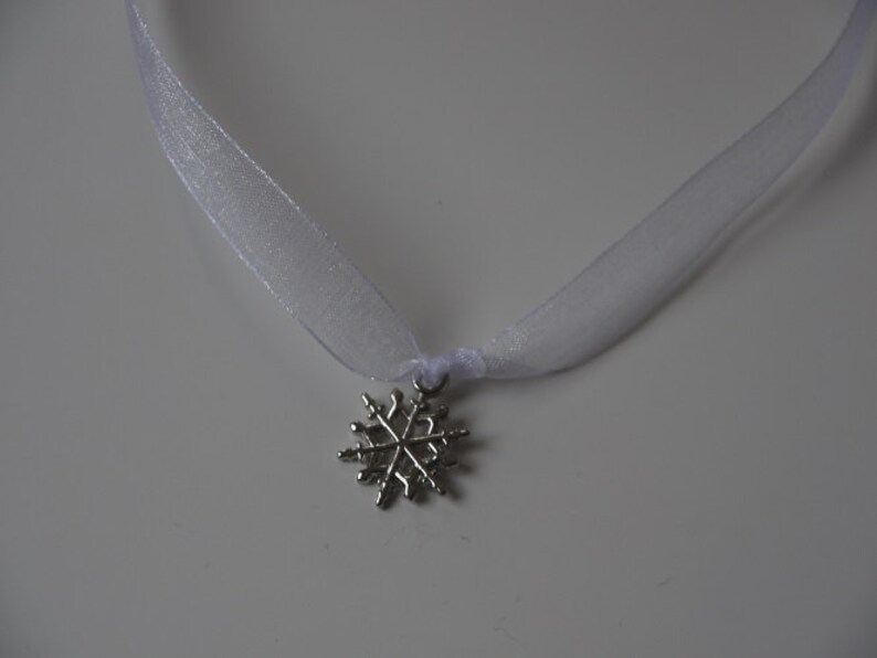 May include: A white ribbon necklace with a silver snowflake pendant.