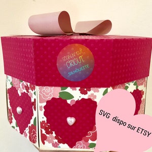Può includere: Una scatola esagonale rosa e rossa con un coperchio a forma di cuore e un motivo floreale. La scatola è decorata con una perla bianca e un fiocco rosa. La scatola ha un adesivo che dice "Scan N' Cut Cricut Silhouette". La scatola è etichettata con "SVG dispo sur ETSY".
