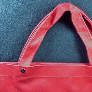 Puede incluir: Bolsa de lona roja con dos asas y remaches met&aacute;licos. La bolsa est&aacute; vac&iacute;a.