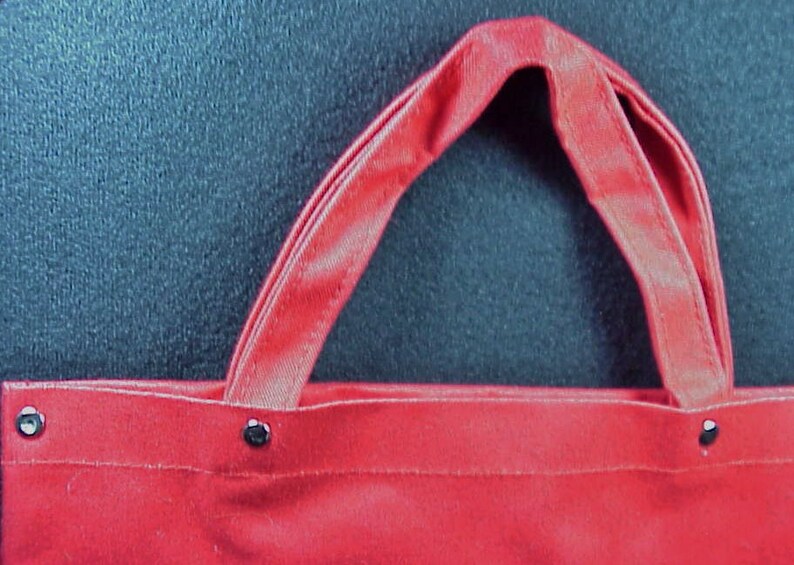 Puede incluir: Bolsa de lona roja con dos asas y remaches met&aacute;licos. La bolsa est&aacute; vac&iacute;a.