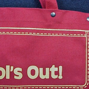Puede incluir: Bolsa de lona roja con costuras blancas y el texto "School's Out!" en amarillo.