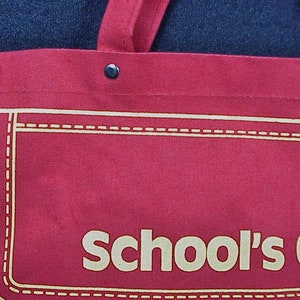 Puede incluir: Bolsa de lona roja con un borde cosido blanco y el texto "School's Out" en blanco.